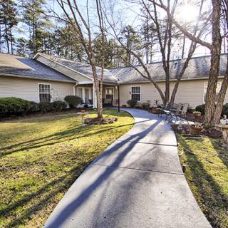 A house with a curved pathway in a sunlit yard surrounded by trees.