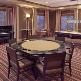 A stylish game room featuring a poker table, pool table, and piano with elegant decor and striped carpeting.