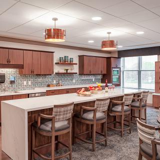 A modern kitchen with a large island and stylish bar stools, featuring wooden cabinets and contemporary lighting.