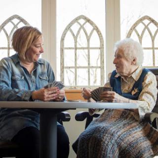 A caregiver enjoys a card game with an elderly woman, highlighting the joy of companionship and social interaction.