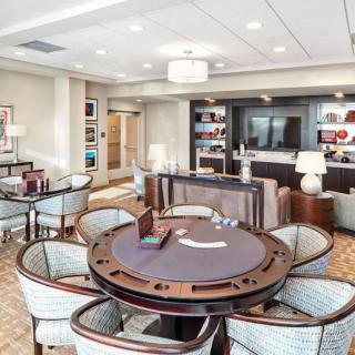 A modern lounge area with a poker table, surrounded by chairs and well-lit bookshelves.