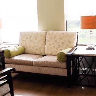 A cozy living room setup featuring a patterned sofa, side tables, and a bright lamp near large windows.