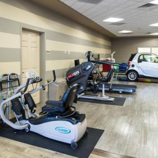 A gym interior featuring various exercise equipment and a parked small car.