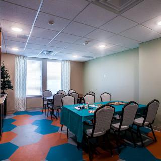 A small meeting room with a conference table and chairs, featuring colorful flooring and large windows.