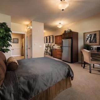 A cozy apartment interior featuring a bedroom with a kitchenette and workspace.
