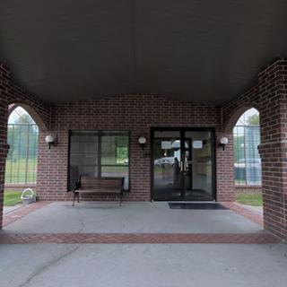 Covered entrance of a brick building with a bench and windows.