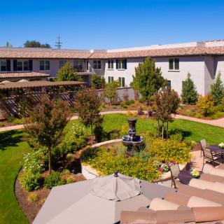 A landscaped courtyard with a fountain, surrounded by outdoor seating and trees on a sunny day.
