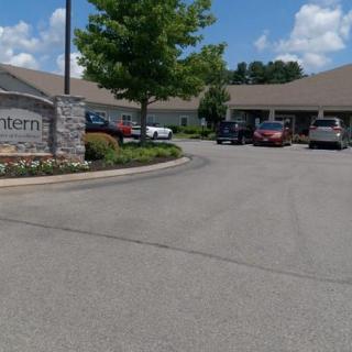 A building with a parking lot and several cars parked in front, under a partly cloudy sky.