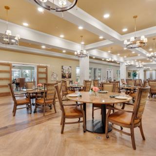 A spacious and elegantly designed dining room with wooden tables and chairs, illuminated by chandeliers.