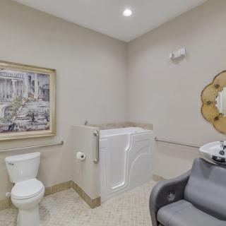A bathroom featuring a walk-in tub, toilet, and salon-style chair with a decorative mirror and framed artwork on the wall.