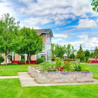 A vibrant garden with raised beds surrounded by lush green grass and trees, under a partly cloudy sky.
