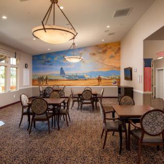 A dining area with tables and chairs, featuring a colorful mural on the wall and warm lighting fixtures.