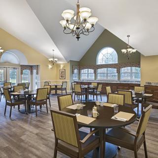 A well-lit dining area with neatly arranged tables and chairs under elegant chandeliers.