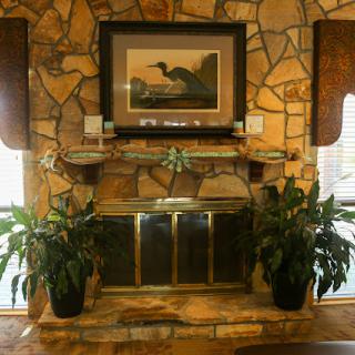 A cozy living room featuring a stone fireplace adorned with plants and an artwork above.
