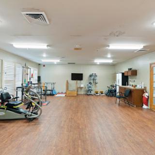 A spacious and well-lit rehabilitation gym equipped with various exercise machines and a wooden floor, ready for fitness activities.