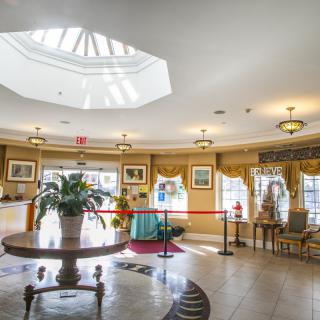 A well-lit lobby interior featuring elegant decor, a central table with a potted plant, and ample natural light from an overhead skylight.