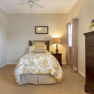 A cozy bedroom with a single bed, nightstand, and dresser, softly lit by a table lamp.