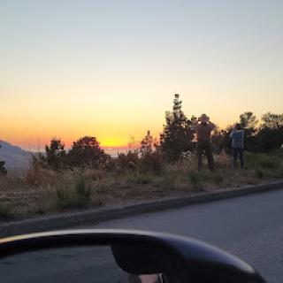 A picturesque sunset viewed from the roadside, with silhouettes of trees and people enjoying the scene.