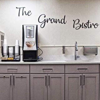 A clean and modern coffee station with the sign 'The Grand Bistro' above, featuring a beverage machine and supplies.