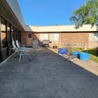 A sunny outdoor patio area with chairs and blue containers next to a building.