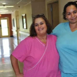 Two healthcare professionals in scrubs smiling in a hospital hallway.