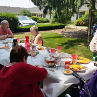 A group of people enjoying a picnic outdoors on a sunny day, with a table full of food and drinks.