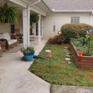 A cozy patio with a raised garden bed filled with plants, surrounded by outdoor seating and vibrant greenery.