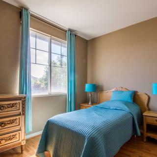 A cozy bedroom with a single bed and blue accents, illuminated by natural light.