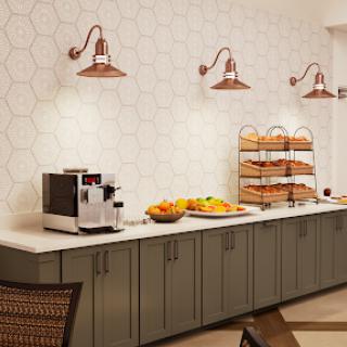 A modern kitchen area featuring a coffee machine, decorative lighting, and a variety of breakfast items displayed.
