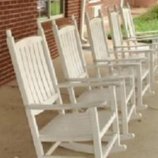 A row of white rocking chairs on a porch.