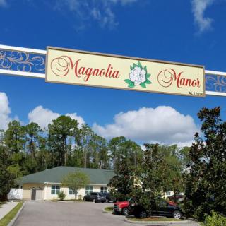 Entrance sign for Magnolia Manor with trees and a building in the background.