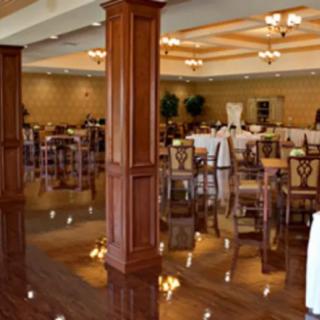 An elegant banquet hall with wooden decor, featuring arranged tables and chairs under warm chandeliers.