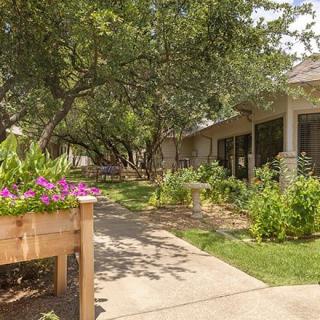 A scenic view of a garden pathway lined with trees and flowers beside a house.