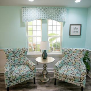 A cozy living room with two patterned chairs, a small round table, and a lamp next to a window.