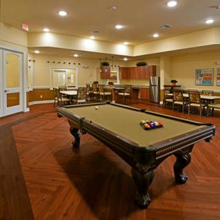 A spacious game room featuring a pool table, surrounded by tables and chairs with warm lighting.