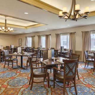 A spacious dining area with multiple tables and chairs, featuring elegant chandeliers and a patterned carpet.