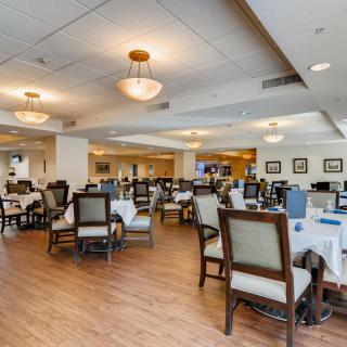 A spacious dining area with multiple tables and chairs, featuring elegant lighting and decor.