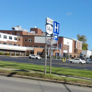A view of a hospital from the road, with clear signs indicating directions.