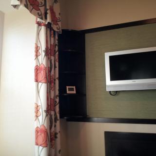 A wall-mounted television in a living room with floral curtains.