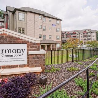 An exterior view of a residential apartment complex with a landscaped garden and signage in the foreground.
