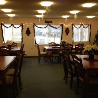 A cozy dining room with multiple tables and chairs, decorated with lights and garlands.