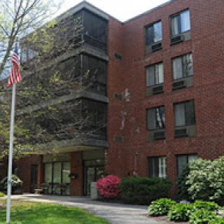A brick building with landscaped greenery and an American flag in front.