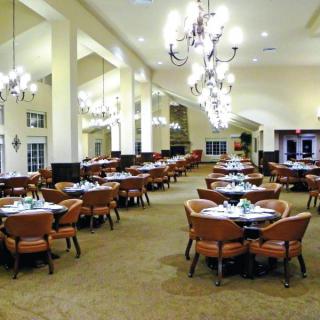 An elegant dining room with neatly arranged tables and chairs, featuring chandeliers and a spacious layout.