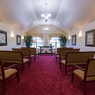 A small chapel interior with rows of seats, red carpet, and decorative elements.
