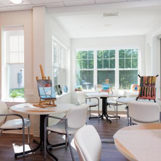 A bright and inviting art room filled with natural sunlight, featuring easels, tables, chairs, and art supplies.