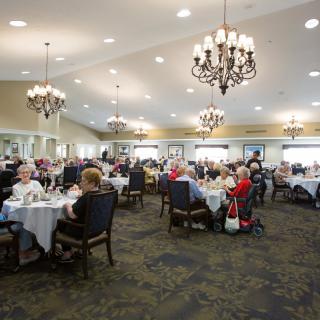 A spacious dining hall with people seated at tables, featuring elegant chandeliers.