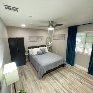 A modern minimalist bedroom featuring a bed with gray bedding, a ceiling fan, and wooden flooring.