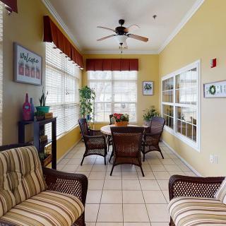 A cozy living area with wicker furniture and a round dining table, surrounded by large windows letting in natural light.