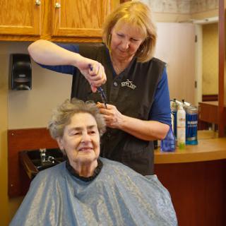A hairdresser styles the hair of a senior woman, creating a moment of care and connection.