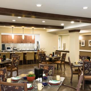 A cozy dining area with elegantly set tables and chairs, featuring an open kitchen design.
